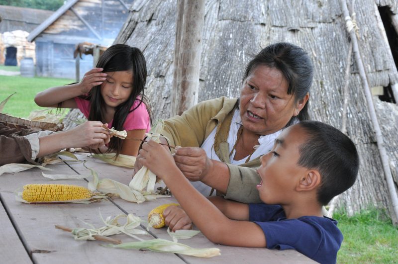 Marilyn, une interprète historique autochtone à Sainte-Marie-au-pays-des-Hurons, enseigne à deux enfants comment faires des poupées avec des épeluches de maïs