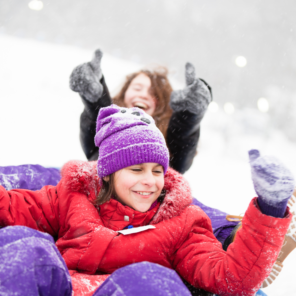 Two girls in winter clothing give the thumbs up after snow tubing down a hill