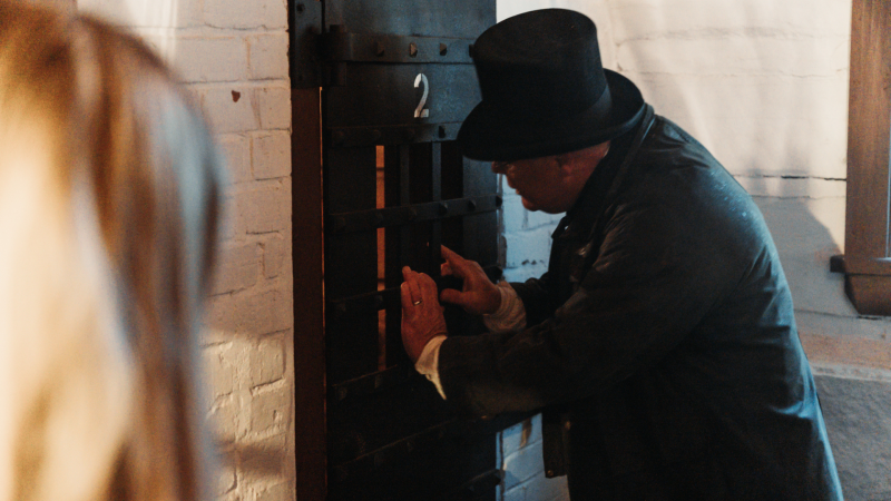 A jail guard peers into a locked cell at the Discovery Harbour Escape Room