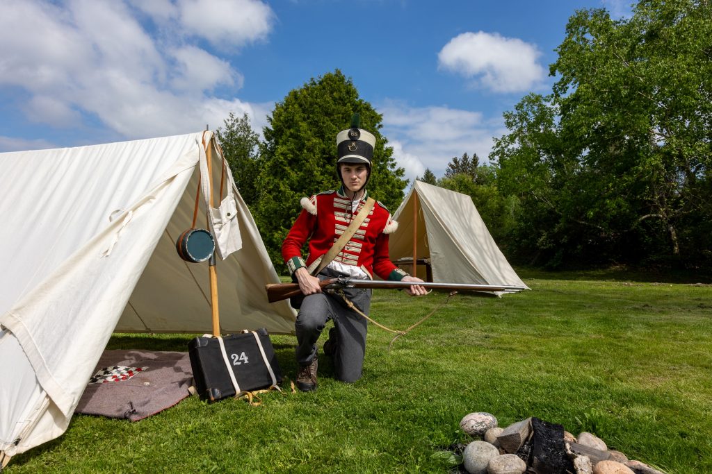 A historical interpreter dressed as a British soldier sitting at an encampment