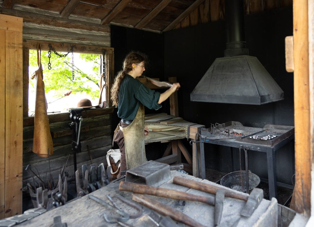 A historical interpreter works in the blacksmith building