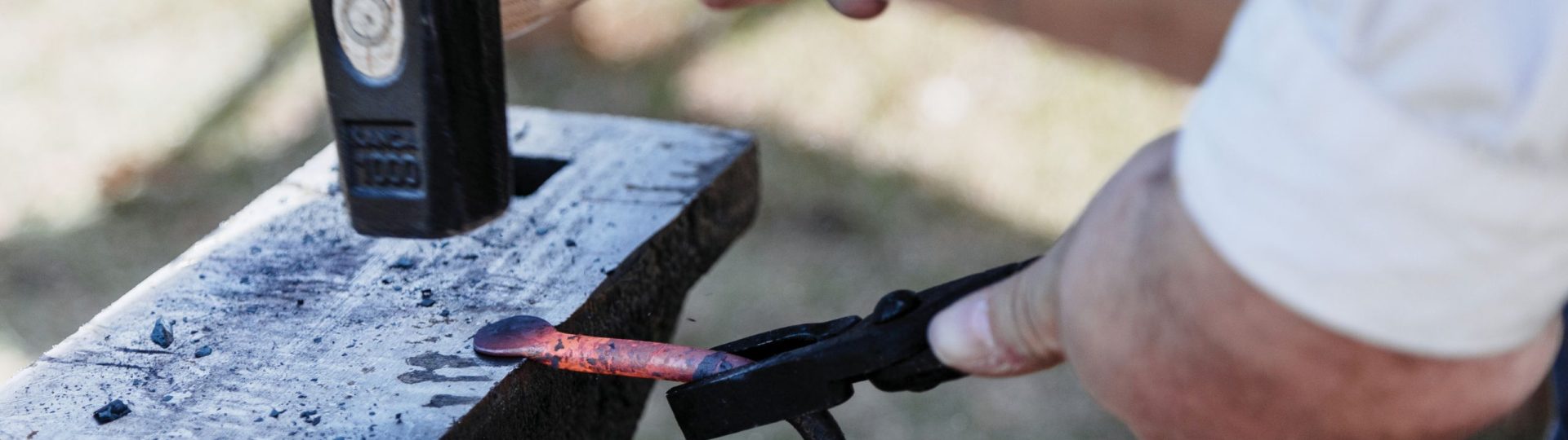 a blacksmith hammering a piece of molten iron into a coathook
